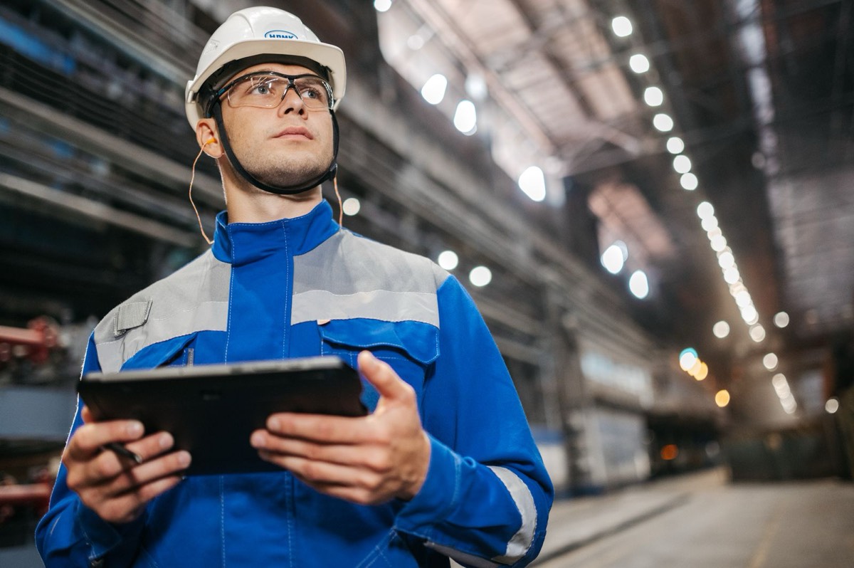 Técnico con casco y ropa de trabajo consultando una tableta en el interior de una planta